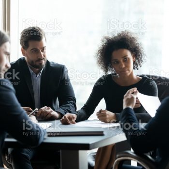 Serious diverse business partners discussing project strategy, contract terms at meeting in boardroom, businesspeople negotiating, colleagues listening to team leader boss at briefing